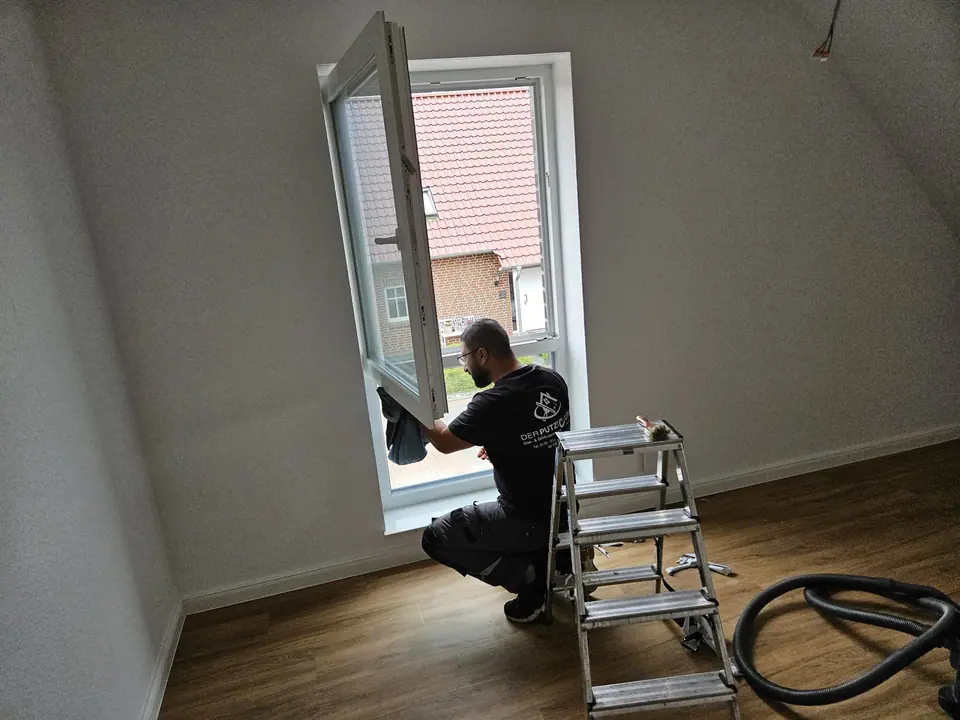 Mitarbeiter reinigt einen Fensterflügel im Neubau, daneben Leiter und Sauger