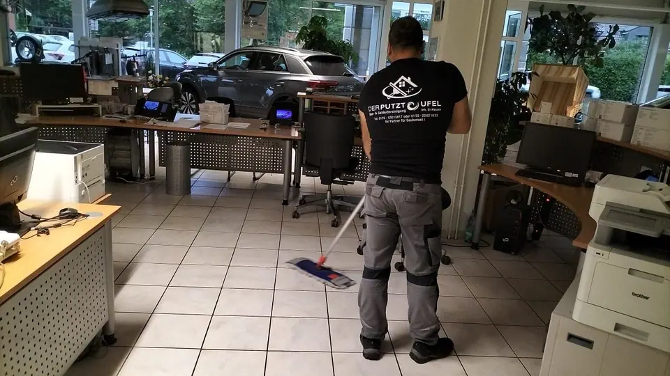 Mitarbeiter wischt den Fliesenboden im Büro eines Autohauses