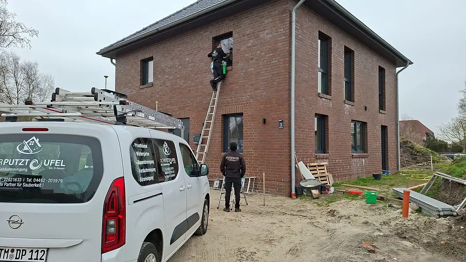 Fensterreinigung an einem Neubau, ein Mitarbeiter auf der Leiter, der Firmenwagen davor