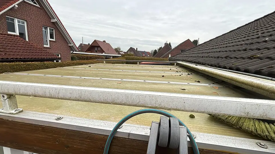 Flaches Terrassendach aus Stegplatten mit grünem Belag vor der Reinigung