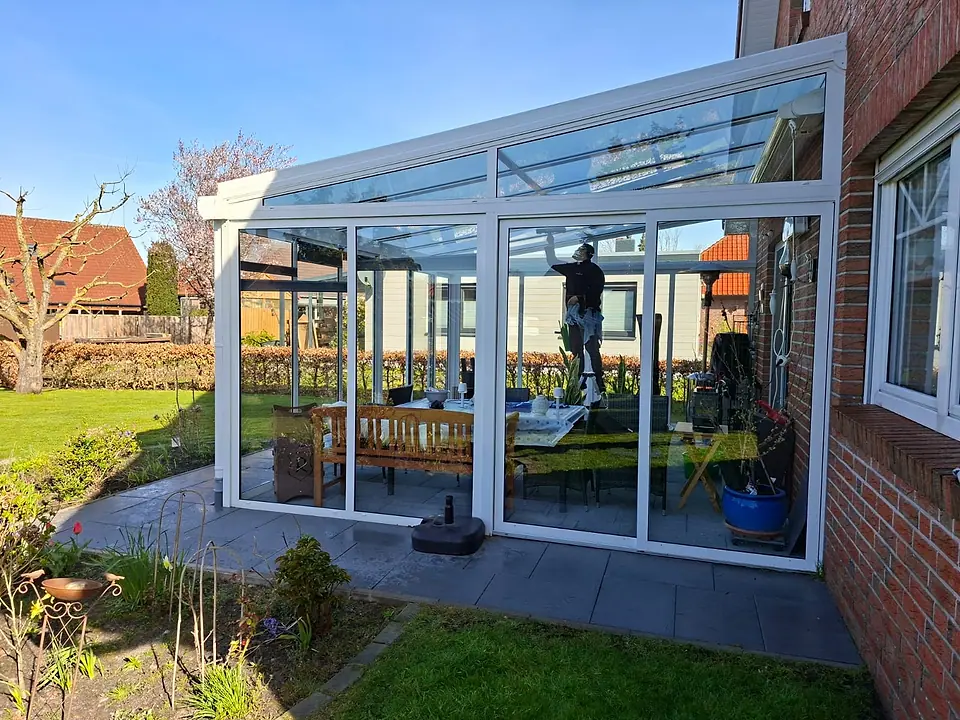 Mitarbeiter steht im Wintergarten auf der Trittleiter und reinigt das Glasdach von innen